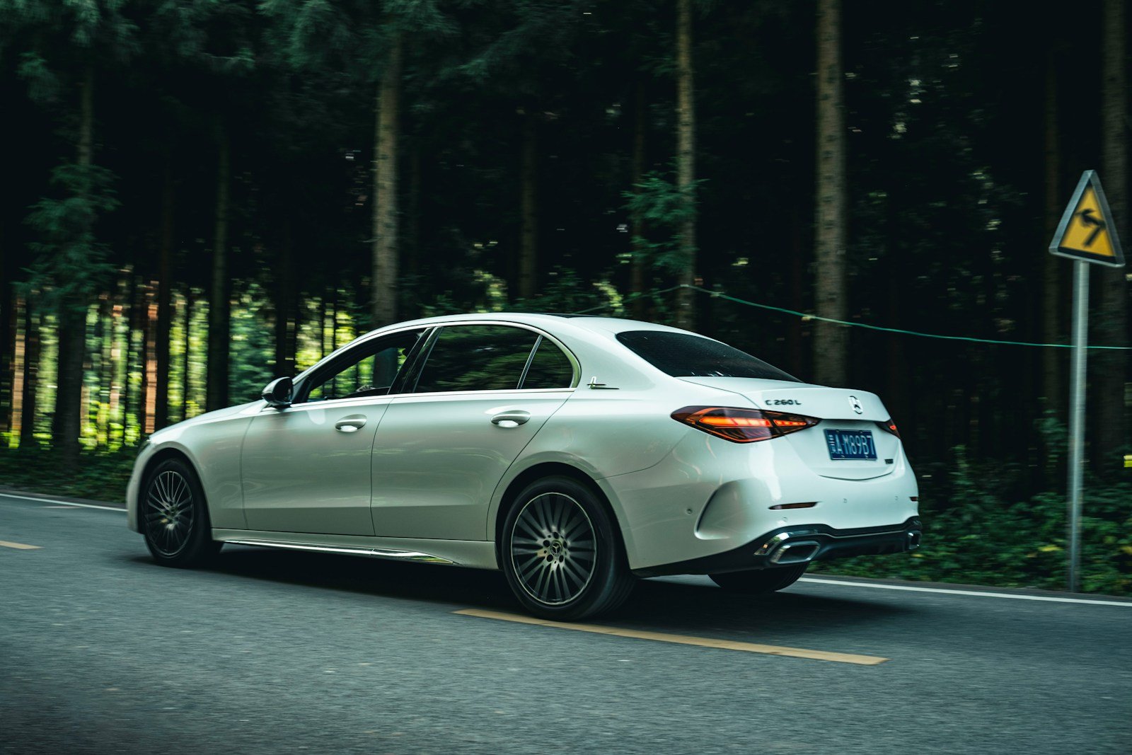 A white car driving down a road next to a forest